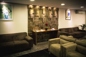 Un área de recepción con diseño moderno, que incluye una pared con diseño, un mostrador de madera y dos sofás.