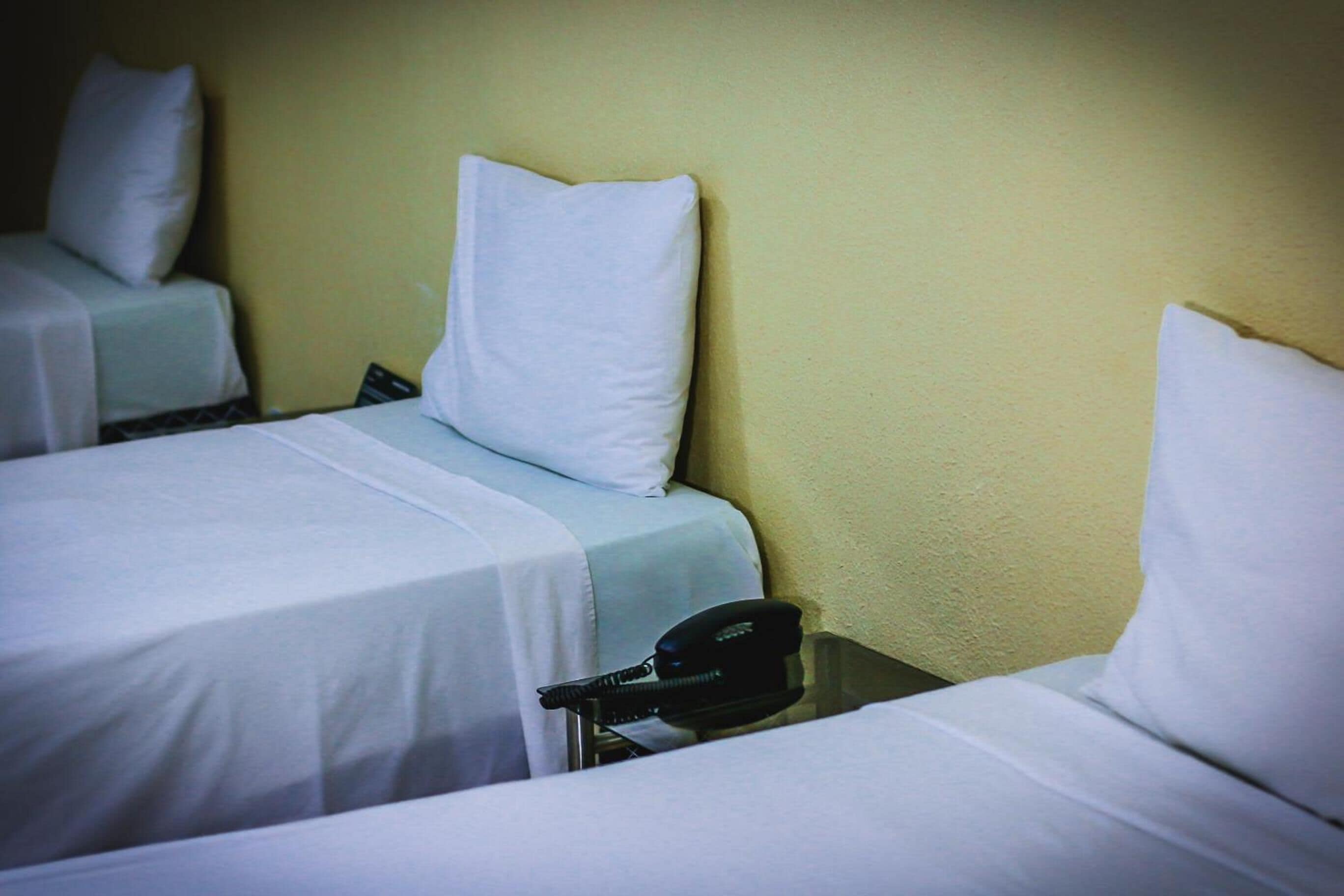 Una habitación de hotel con dos camas, cada una con una almohada y una manta. Hay un teléfono en la mesita de noche.