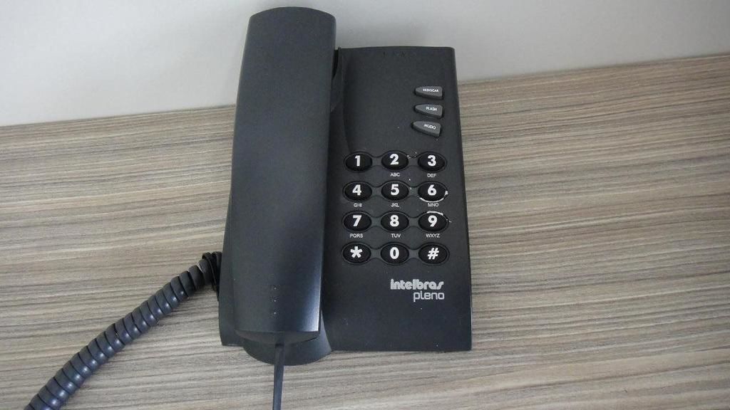 A black telephone with a cord on a wooden surface.