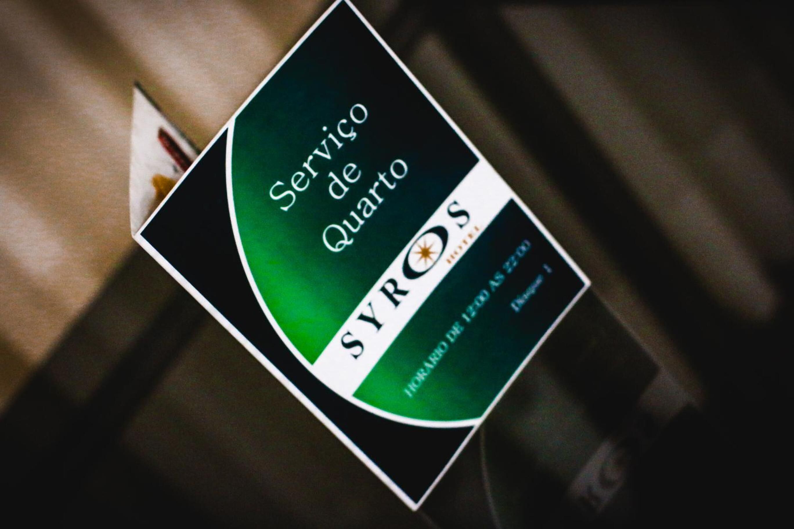 Un letrero en una habitación de hotel con el texto 'Serviço de Quartos SYROS' y 'HORA DE IZERDA AS 22:00'.