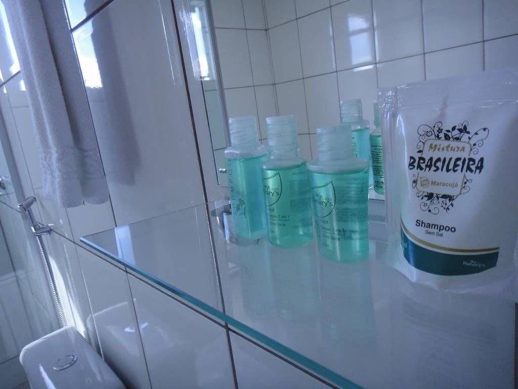 A bathroom with a glass shower enclosure, a white sink, and a bottle of shampoo on the counter.