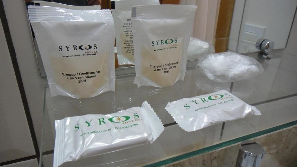 A bathroom counter with toiletries including shampoo and conditioner from SYROS HOTEL.