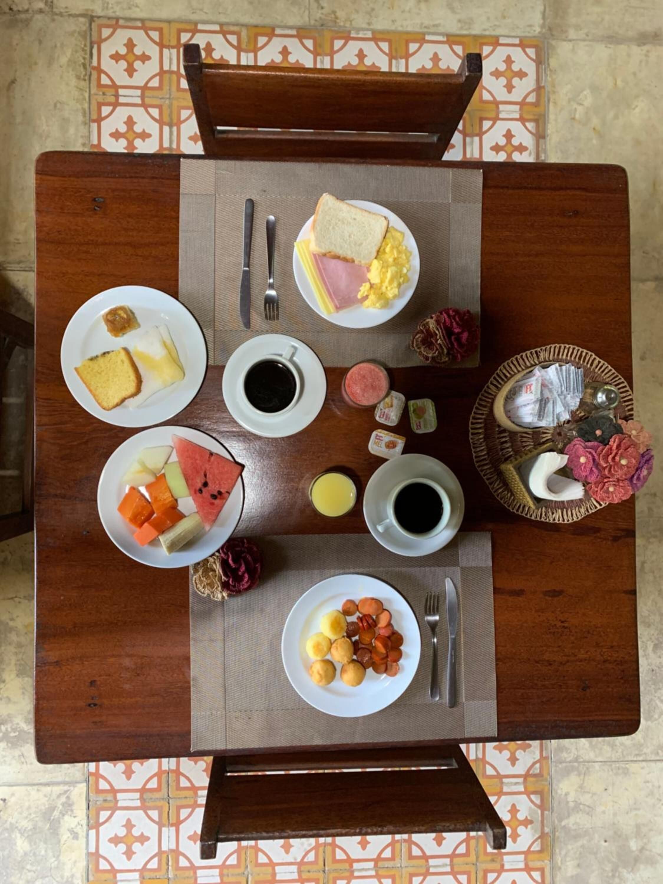 Une table à manger avec divers aliments pour le petit-déjeuner, notamment des toasts, des œufs, du jambon et des fruits.