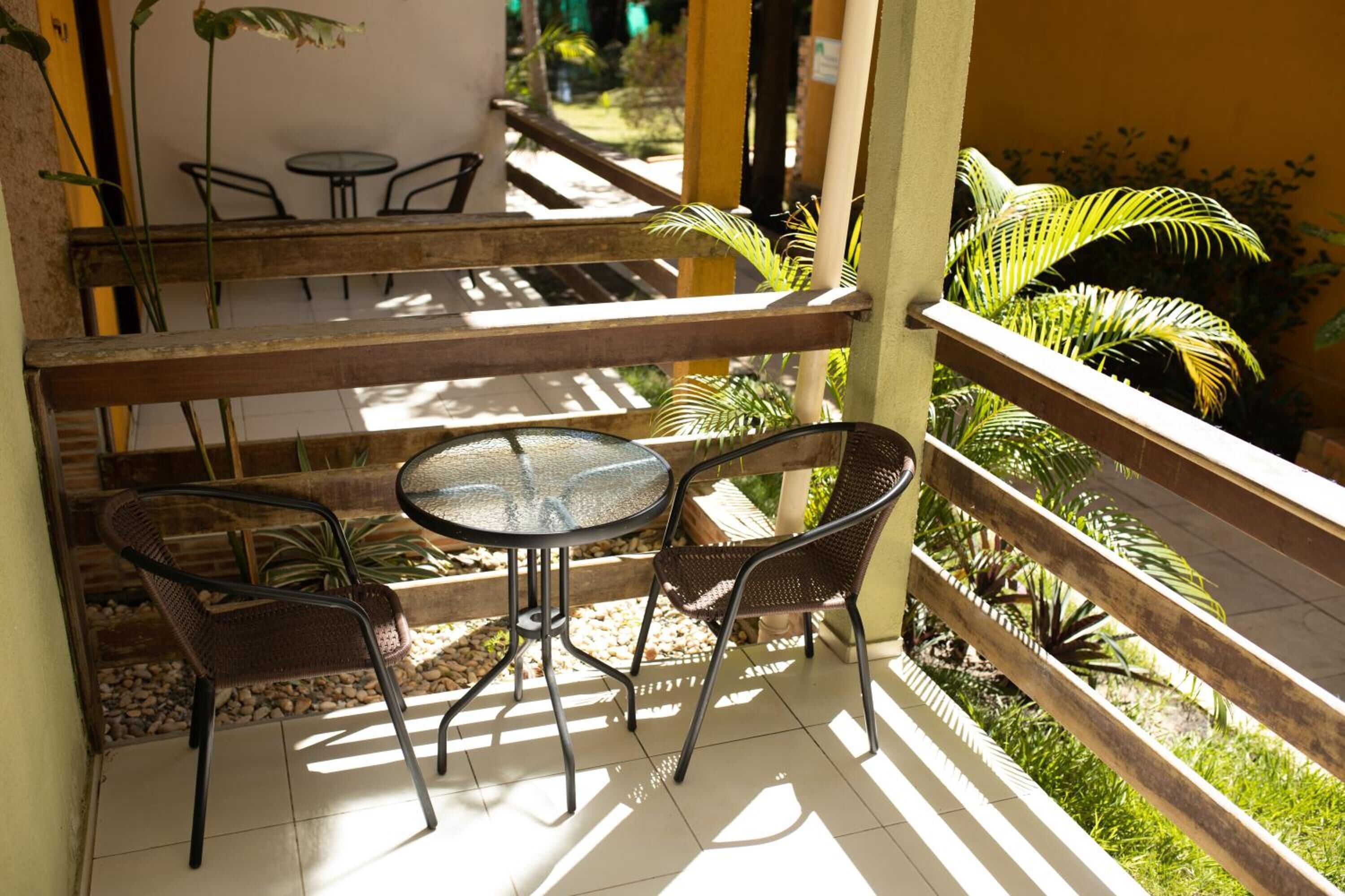 A balcony with a table and chairs, surrounded by plants and a wooden railing.