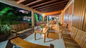 Un espace extérieur aménagé en terrasse, avec des meubles en bois, notamment des bancs et des tables, entouré de plantes en pot.