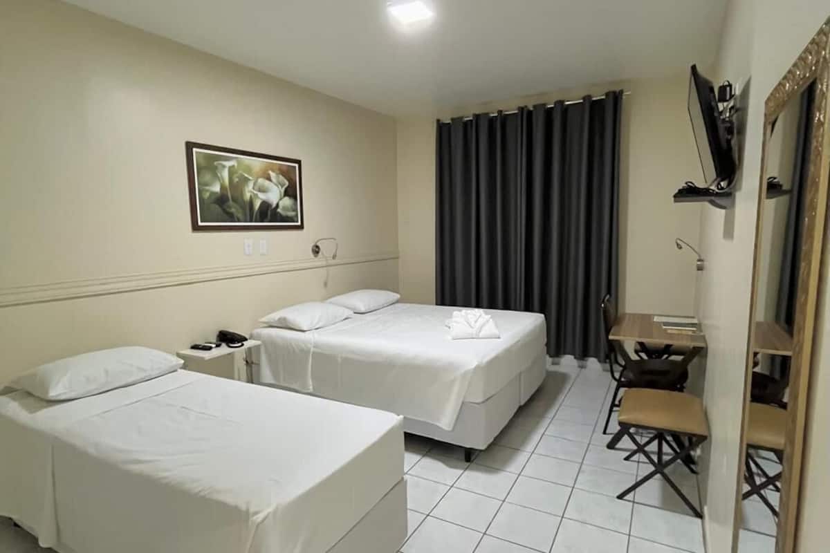 A hotel room with two single beds, a small table, a chair, a desk, a television, and a mirror.