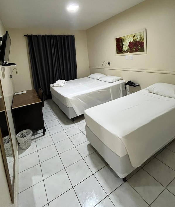 A hotel room with two single beds, a desk with a chair, a small trash bin, and a painting on the wall.