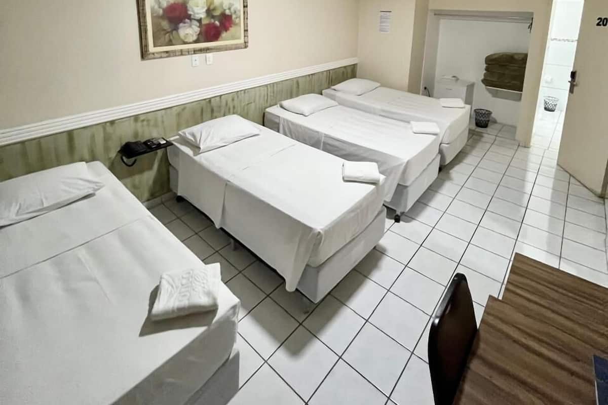A hotel room with three single beds, a wooden table, a painting on the wall, and an air conditioning unit.