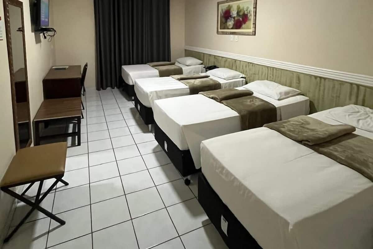 A hotel room with four single beds, a desk with a chair, a television, and a painting on the wall.