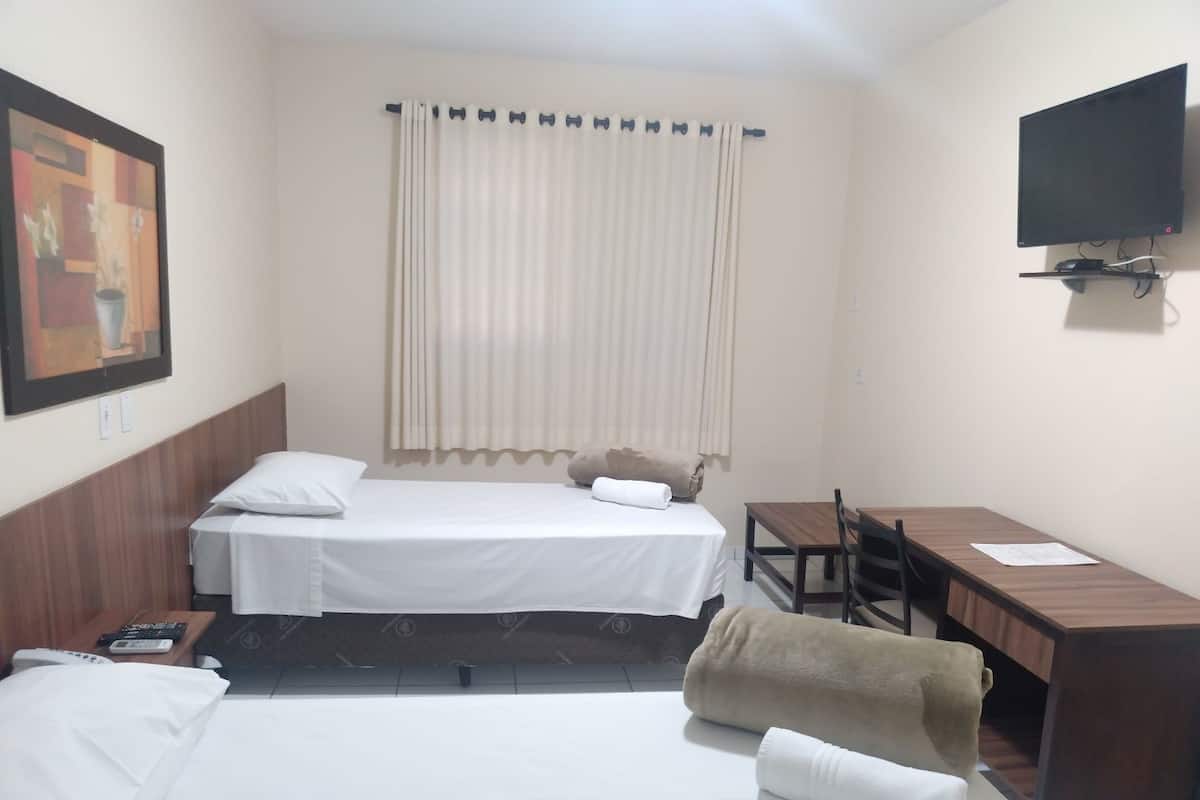 A hotel room with two beds, a desk, a chair, a television, and a painting on the wall.