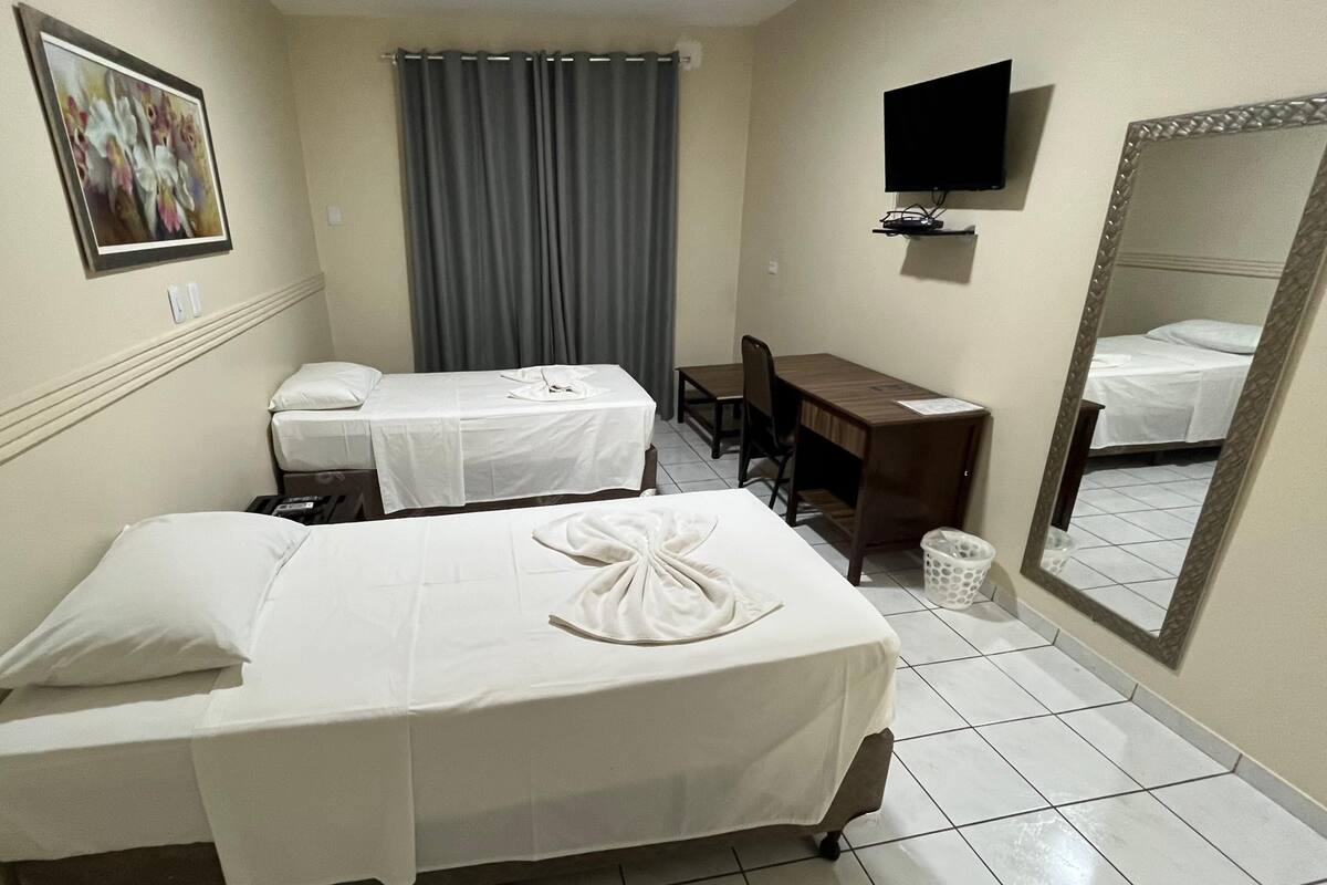 A hotel room with two beds, a desk, a chair, a television, a mirror, and a curtain.