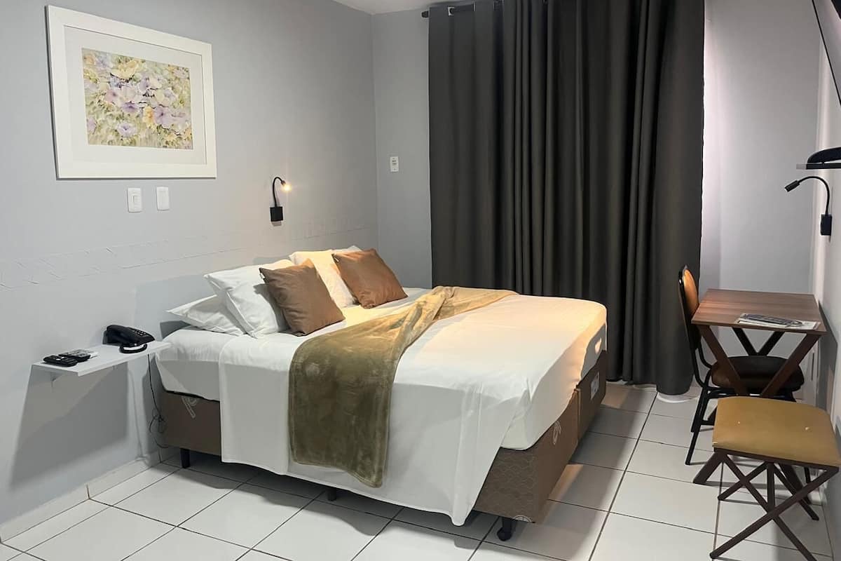 A neatly arranged bedroom with a bed, bedside table, and a small desk with a chair.