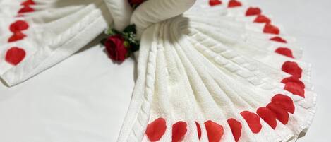 A bed with white linens, a heart-shaped towel arrangement, and red rose decorations.