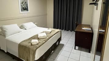A hotel room with a bed, a desk, a mirror, and a picture on the wall.