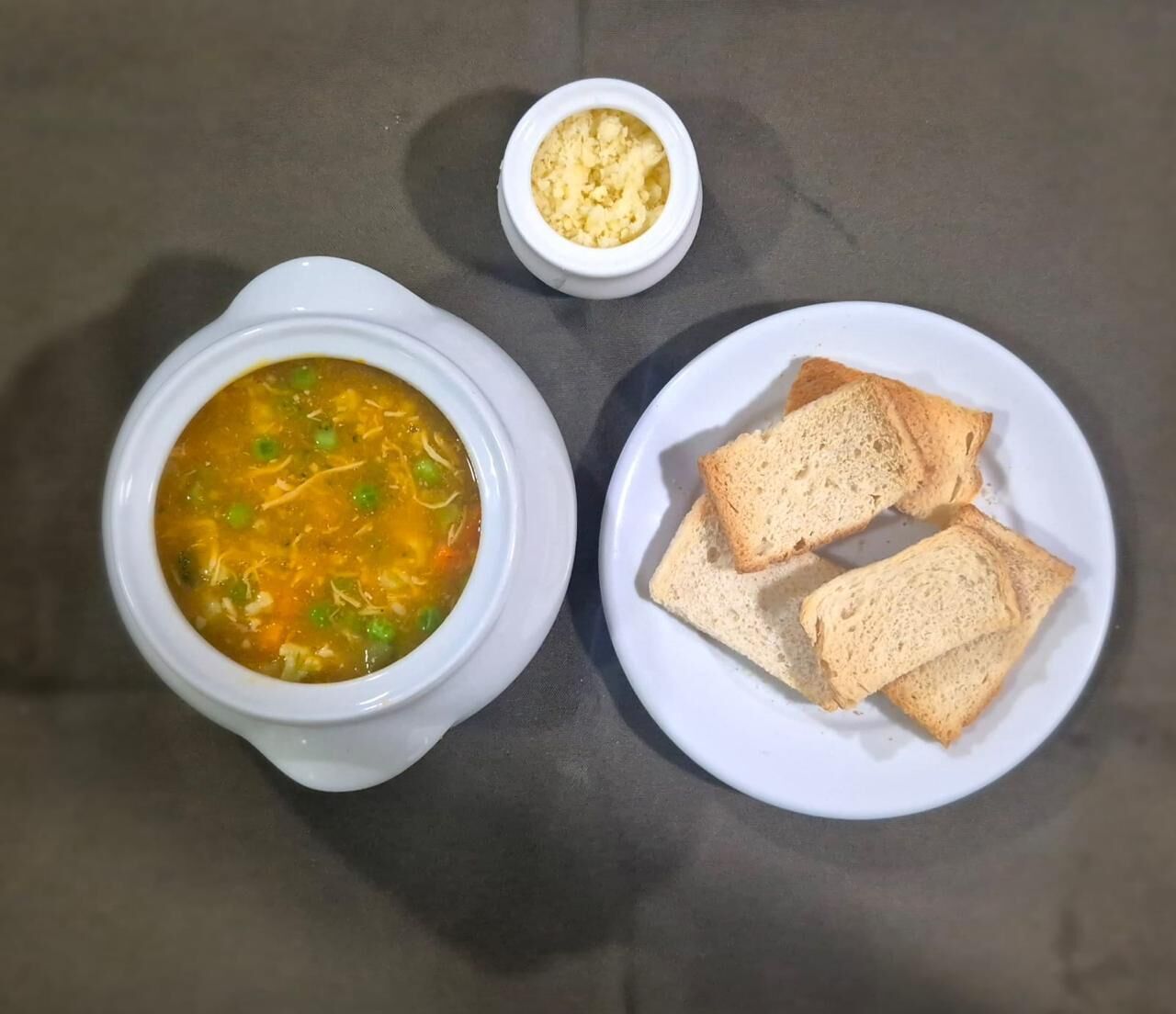 A bowl of soup with vegetables and a plate of bread.