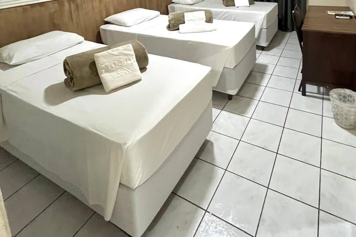 A hotel room with three single beds, a wooden headboard, a flat-screen TV, a desk, and a small table.