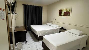 Een hotelkamer met twee eenpersoonsbedden, een bureau, een stoel, een spiegel, een prullenbak en een schilderij aan de muur.