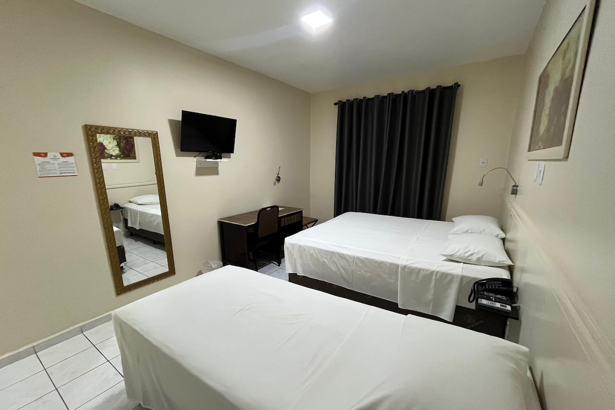 A hotel room with two single beds, a desk, a chair, a television, and a mirror.
