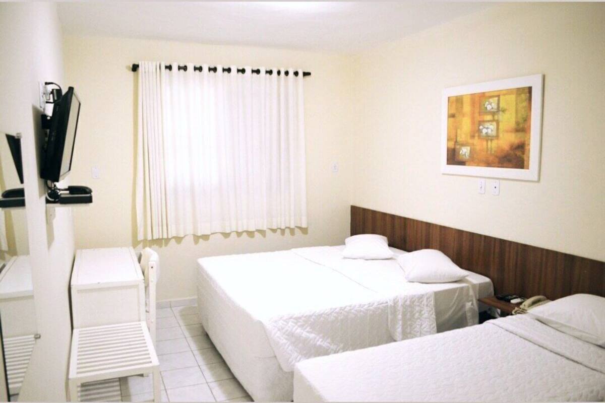 A hotel room with two beds, a desk, a chair, a window with curtains, and a painting on the wall.