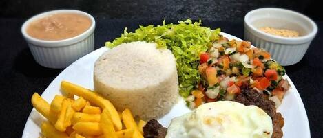 Un plato de comida con bistec, papas fritas, arroz, ensalada y dos salsas para mojar.