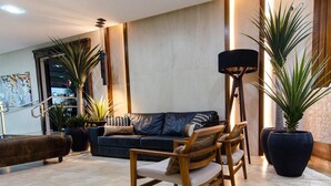 Un lobby moderno con un sofá de cuero oscuro, sillas de madera y plantas de gran tamaño.