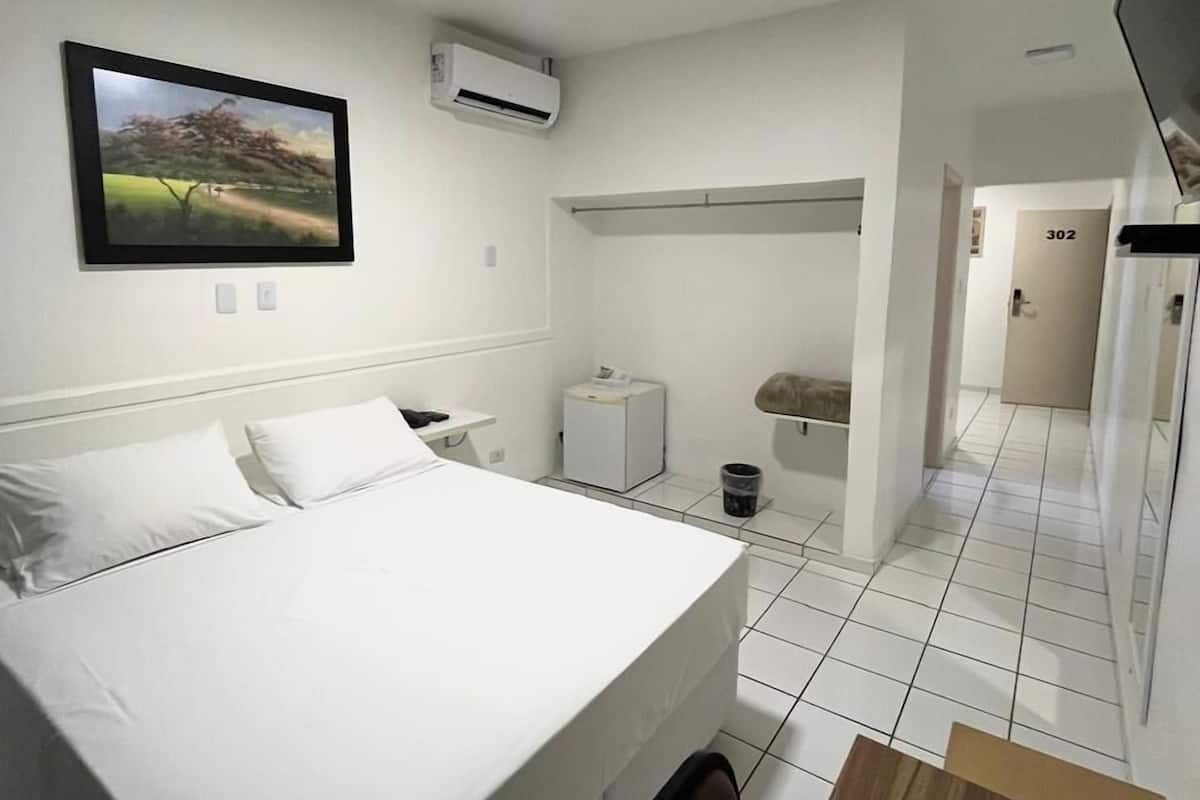 A hotel room with a bed, a desk, a television mounted on the wall, an air conditioning unit, and a door labeled "302".