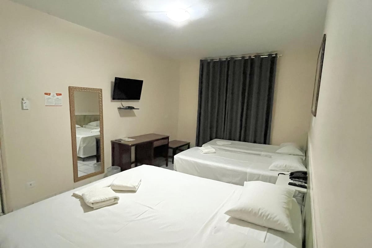 A hotel room with two beds, a desk, a chair, a television, and a window with curtains.