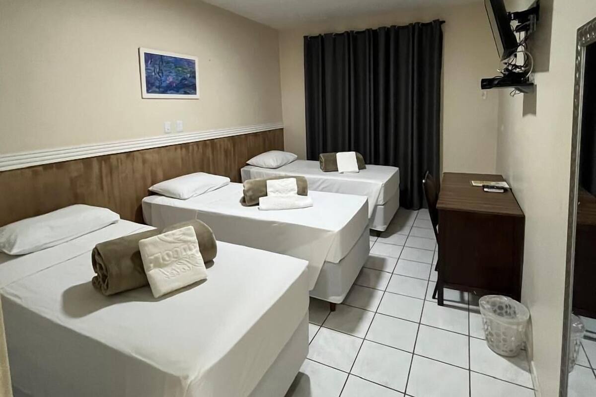 A hotel room with three beds, a desk, a chair, a television, and a picture on the wall.