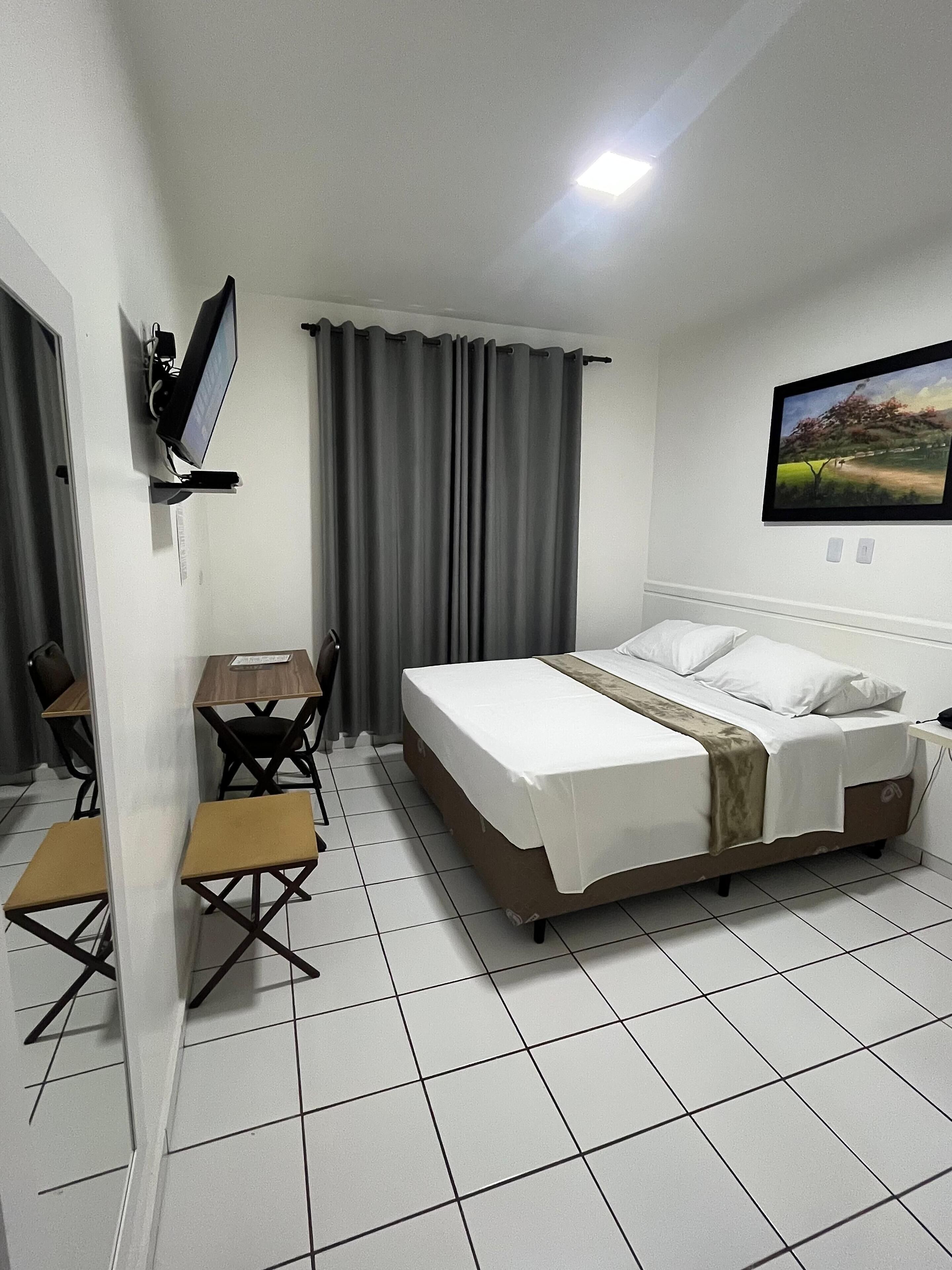 Une chambre d’hôtel avec un lit, un bureau, une chaise, un téléviseur fixé au mur et un tableau.