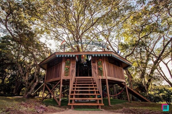Uma casa na árvore de madeira com uma escada que leva até ela, cercada por árvores.