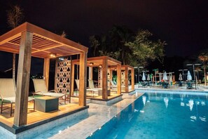A nighttime poolside area with wooden pergolas, lounge chairs, and umbrellas. - Hotel Pousada do Bosque (Ponta Porã)