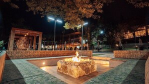 Un espacio de estar al aire libre con un pozo de fuego de piedra, rodeado de cojines estampados y bajo un árbol.