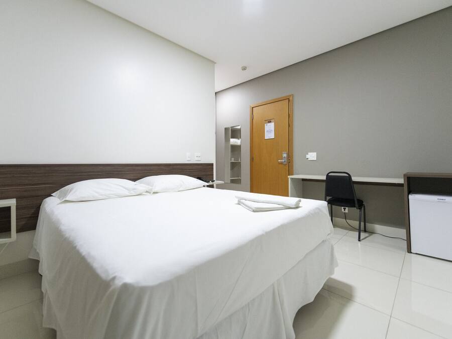 Habitació d'hotel amb llit, escriptori, cadira i nevera petita.