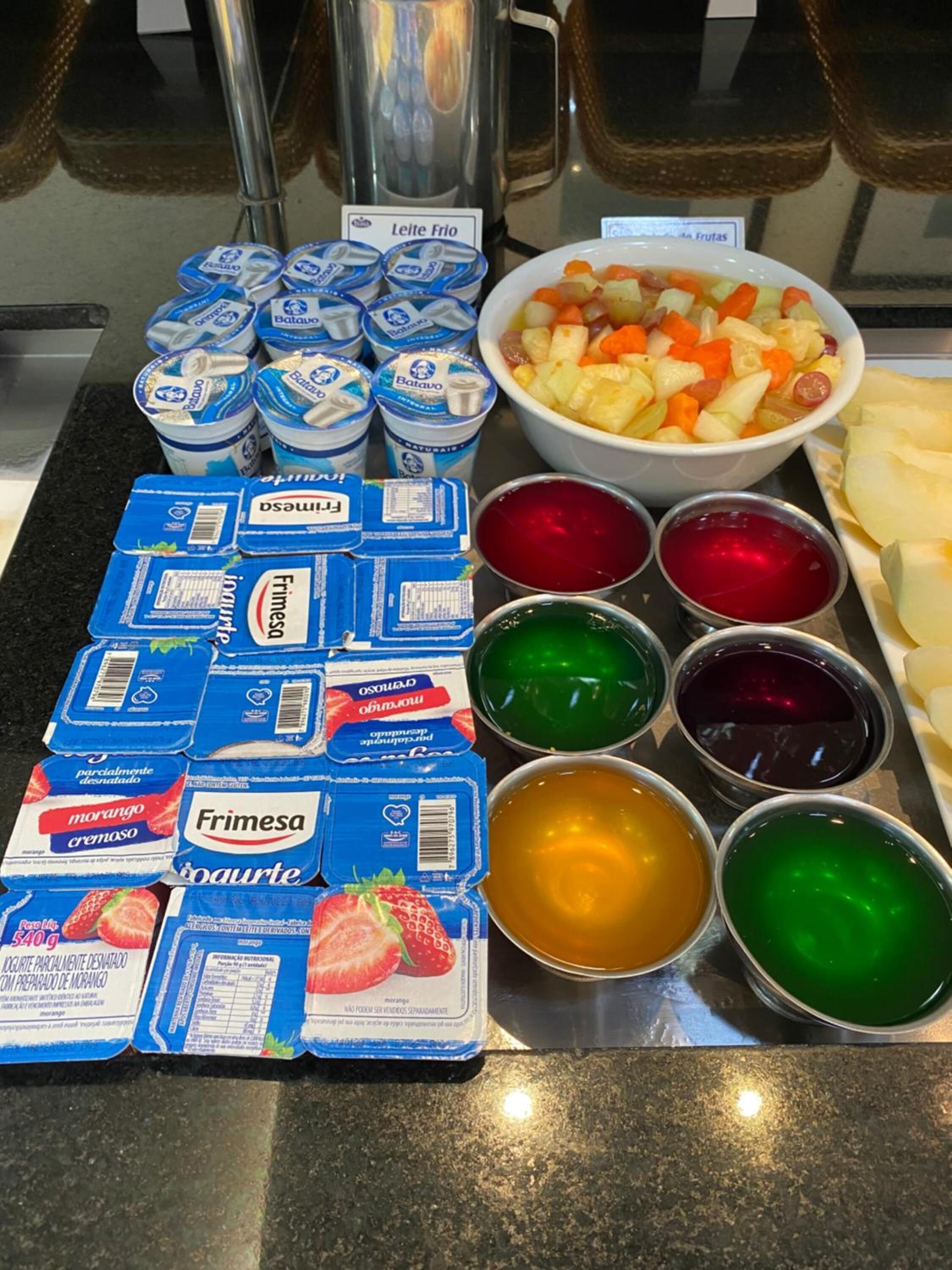 A buffet table with various dairy products, including yogurt and cheese, and a bowl of fruit salad.