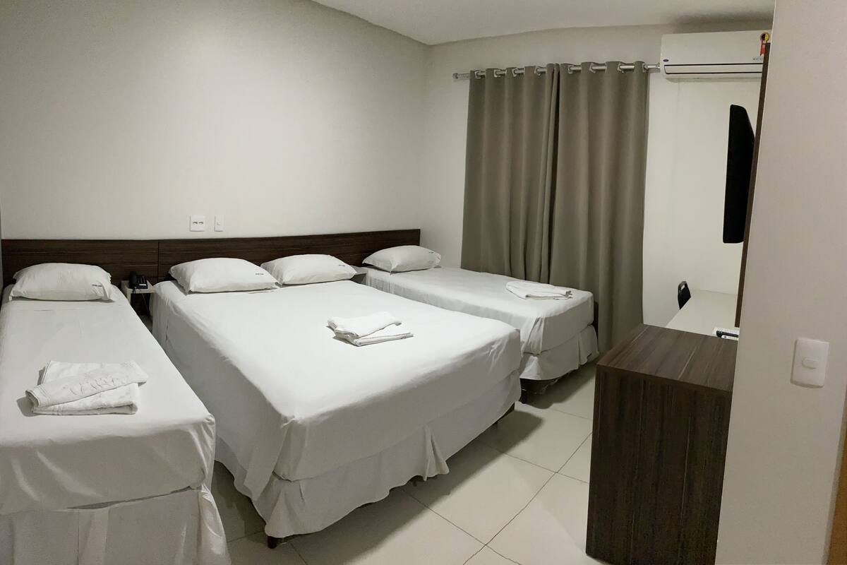 A hotel room with three single beds, a wooden headboard, a bedside table with a phone, and a bathroom with a shower curtain.