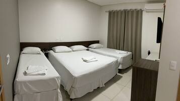 A hotel room with three single beds, a wooden headboard, a bedside table with a phone, and a bathroom with a shower curtain.