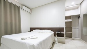 A hotel room with a bed, a bedside table, a wardrobe, and a bathroom. - Hotel Tainá - Aeroporto Cuiabá (Varzea Grande)