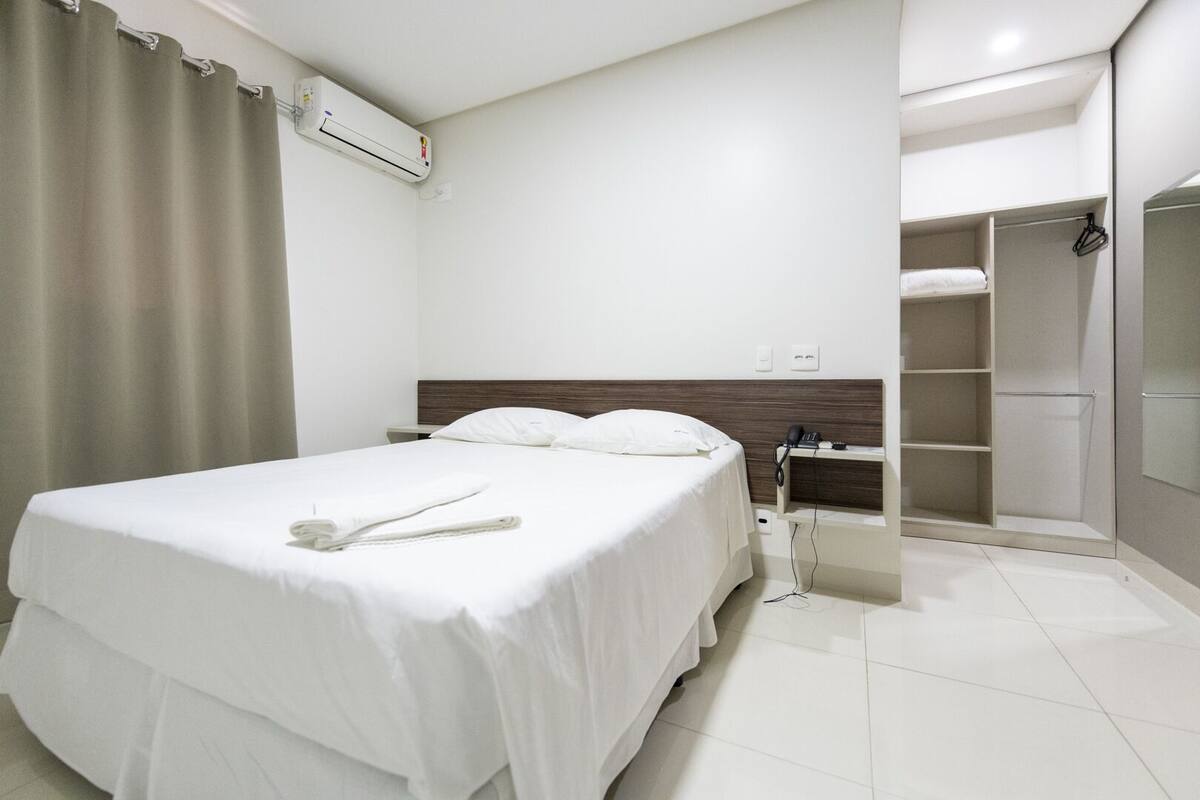 A hotel room with a bed, a bedside table, a wardrobe, and a bathroom.