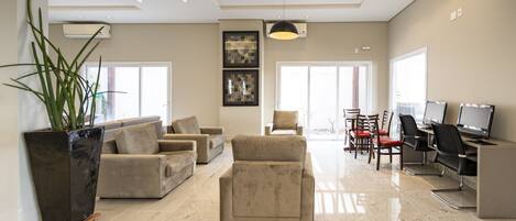 A modern living room with a sofa set, a coffee table, and a dining area with chairs and a table. There is a large window providing natural light and a view outside.