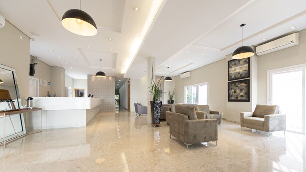 A spacious lobby with a reception desk, seating area, and a modern kitchen in the background. - Hotel Tainá - Aeroporto Cuiabá (Varzea Grande)
