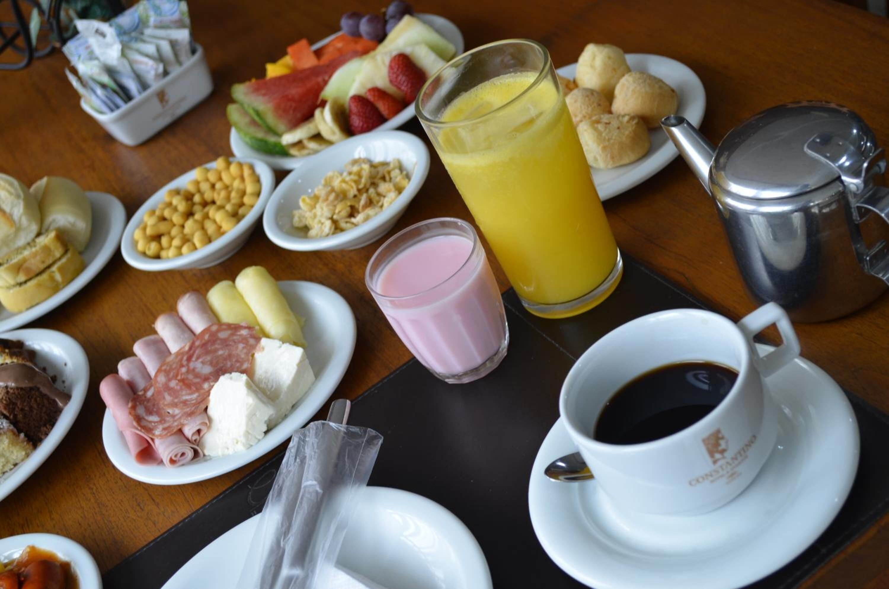 Una mesa de desayuno con diversos alimentos, un vaso de zumo de naranja, una taza de café y una tetera.