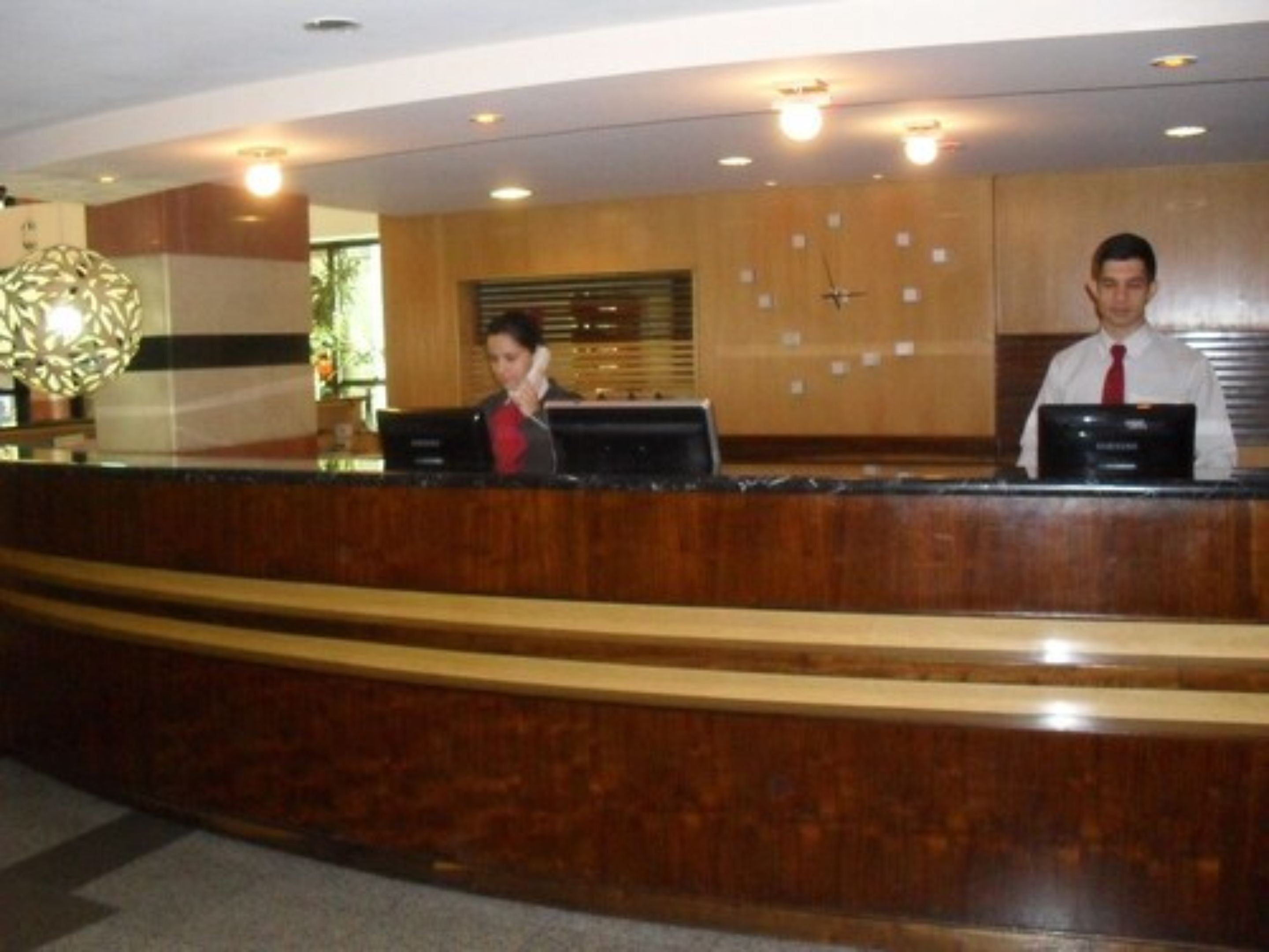 A reception desk with two staff members, a clock, and a decorative wall piece.