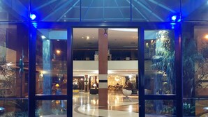 A hotel lobby with a glass entrance, a central column, and a fountain. - Constantino Hotel (Juiz de Fora)