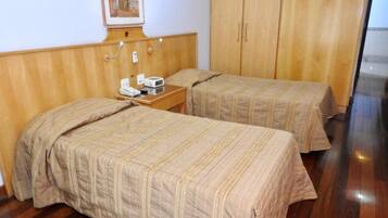 A hotel room with two beds, wooden headboard, a bedside table with a phone and radio, and a framed picture on the wall.