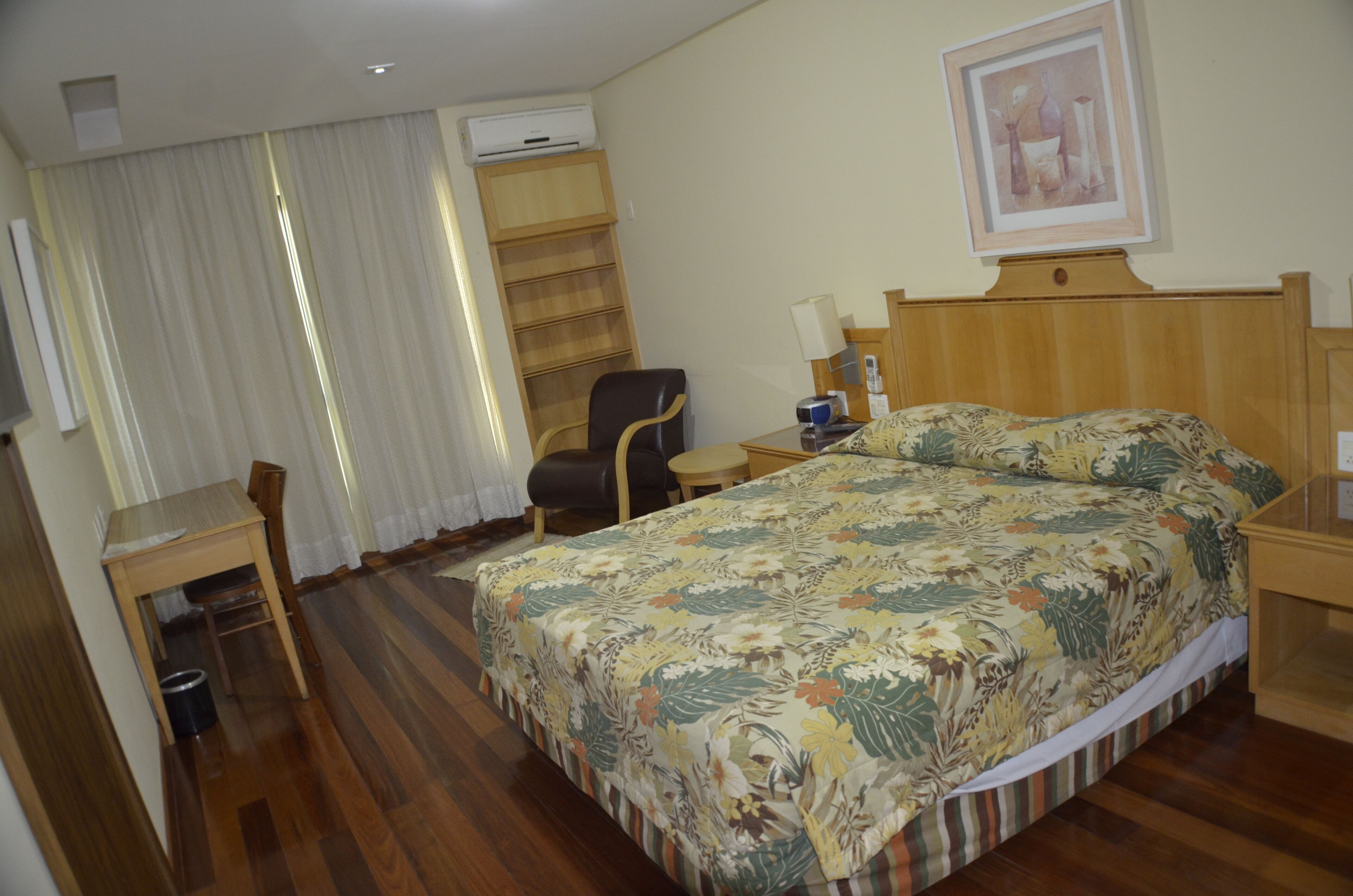 A hotel room with a bed, a desk, a chair, a small table, and a window with curtains.