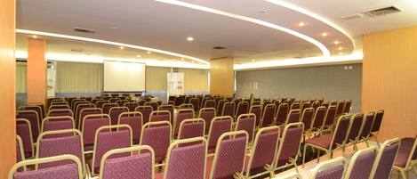 Un salón de conferencias con filas de sillas moradas y una pantalla de proyección grande.