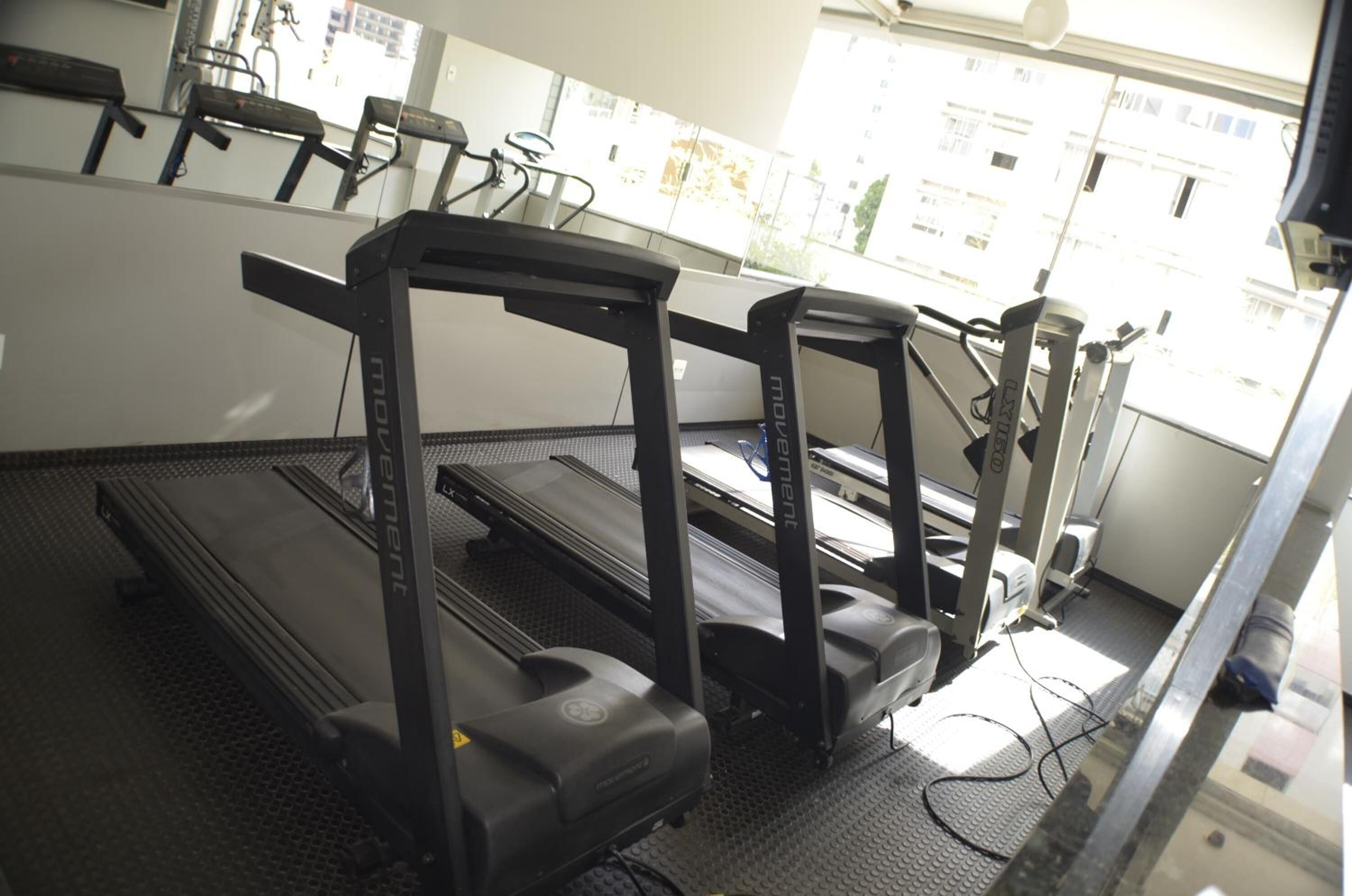 Tres cintas de correr en un gimnasio con vista a la ventana.