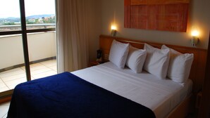 Habitación de hotel con una cama grande, vista de la ciudad por la ventana y un cuadro en la pared.