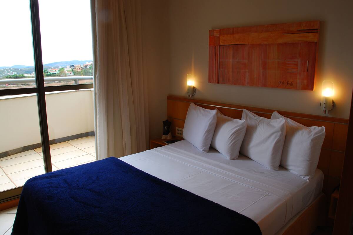 Une chambre d’hôtel avec un grand lit, une vue sur la ville par la fenêtre et un tableau au mur.