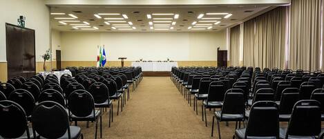 Un salón de conferencias con filas de sillas negras, un atril y banderas.